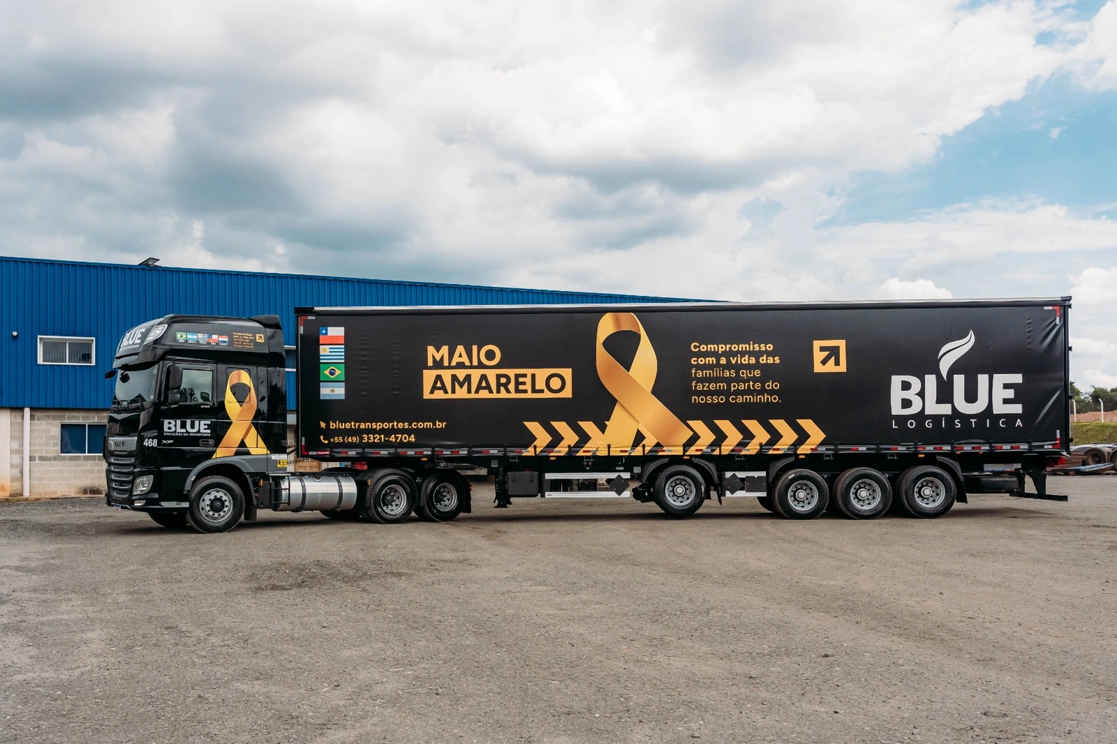 Caminhão DAF preto da BLUE com carreta lonada preta da campanha Maio Amarelo, com laço amarelo e a frase sobre compromisso com a vida.