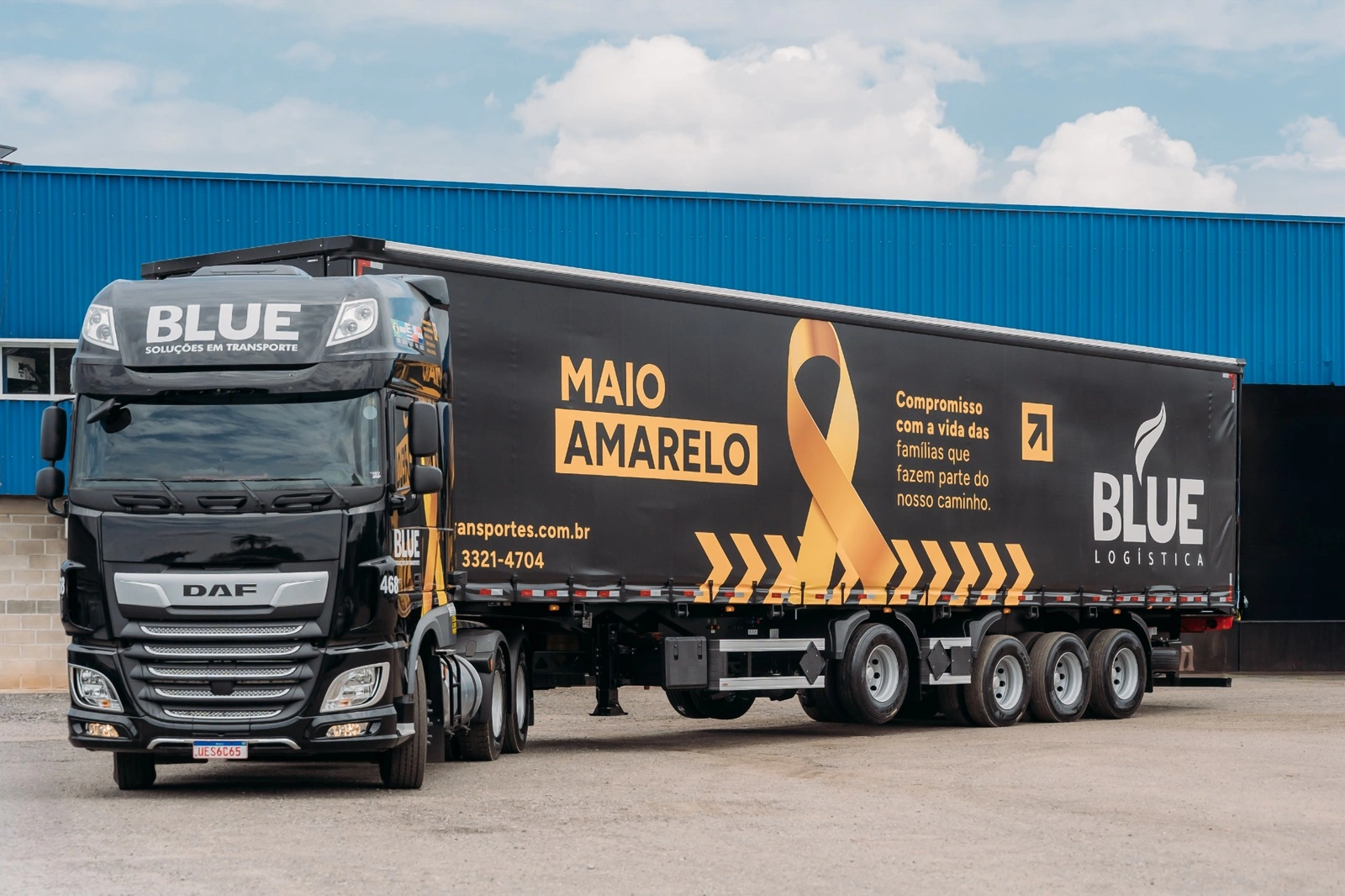 Frente do DAF 468 com a carreta Maio Amarelo diante do galpão azul.
